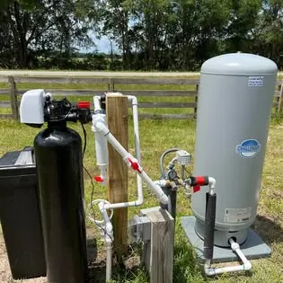 A pressure tank and treatment tank plumbed beside a fence post at a pasture