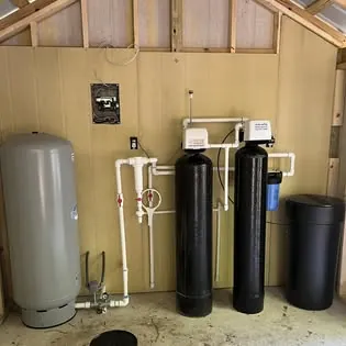 A pressure tank, two treatment tanks and a brine tank inside a wooden well shed
