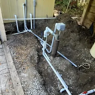 New PVC water lines and a well head in a freshly dug trench beside a shed